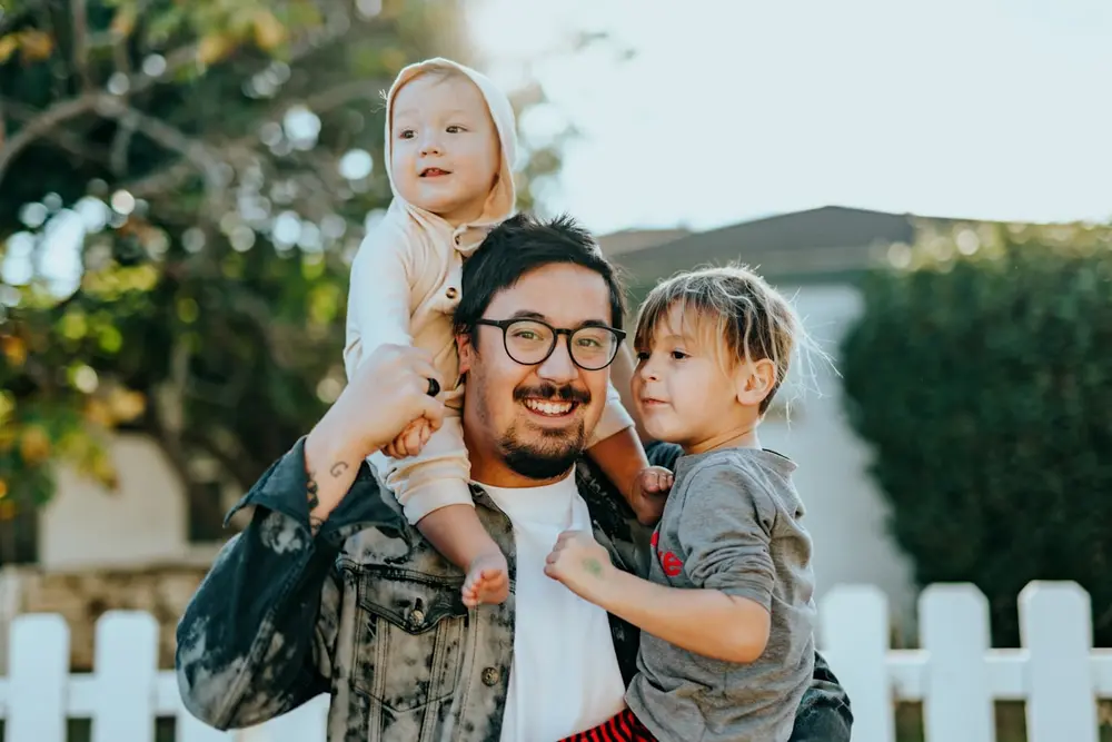 Dad carrying his two kids in front of their home